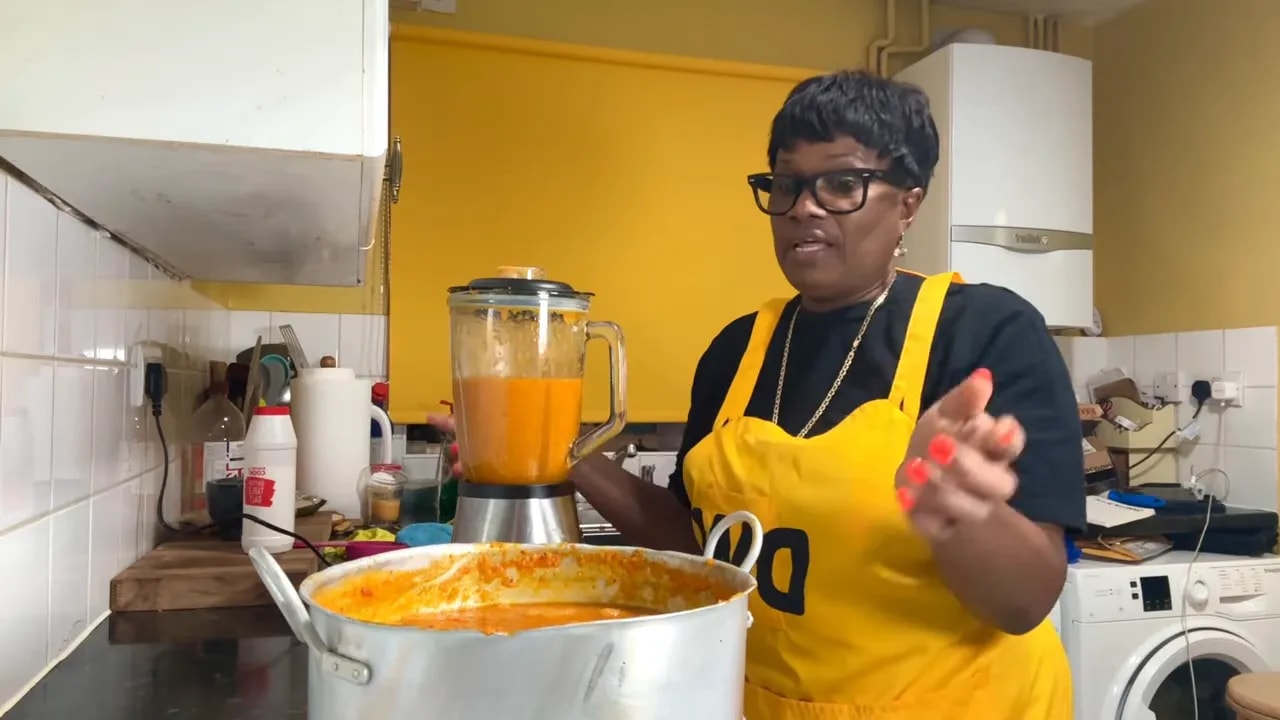 Donna speaking next to a large pot of simmering orange pepper sauce for Jamaican style habanero sauce