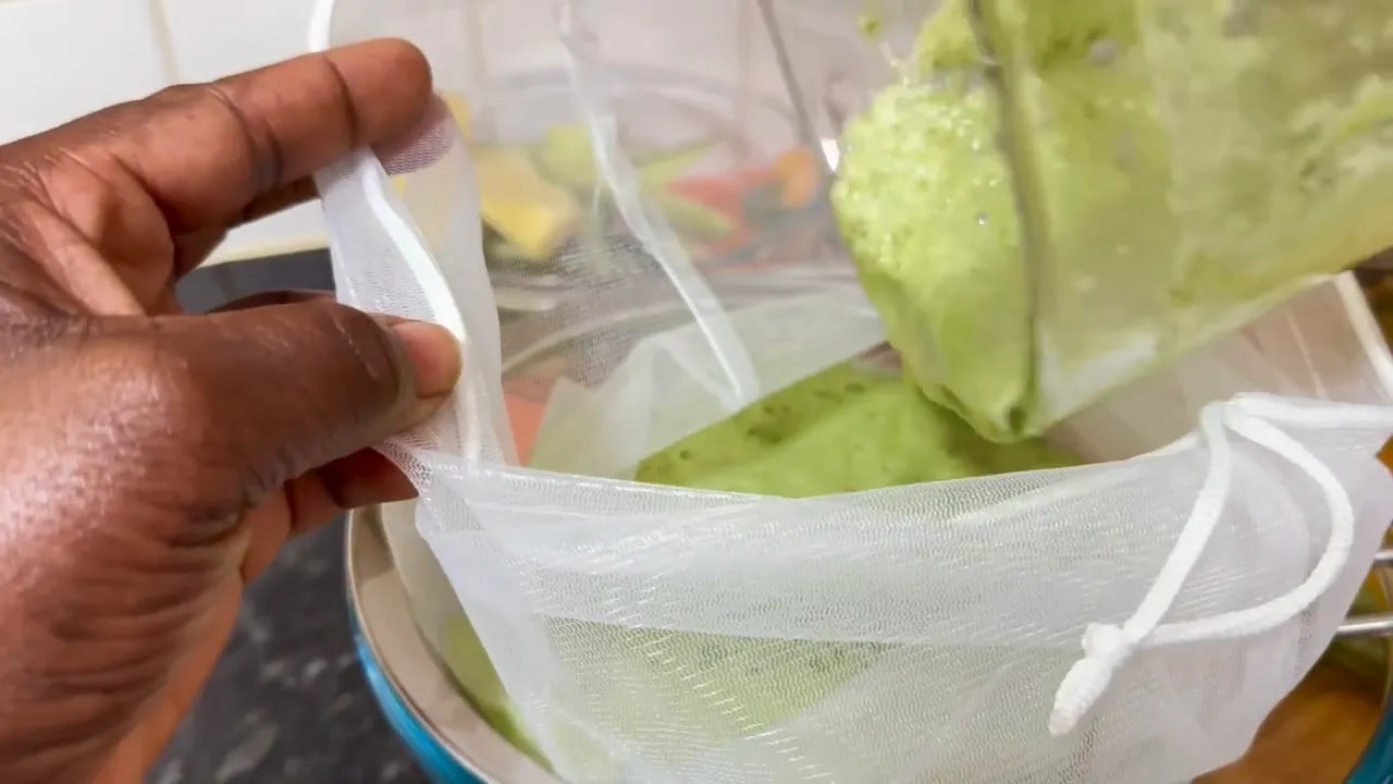 Blended green bitter melon mixture being poured into a bag-lined strainer